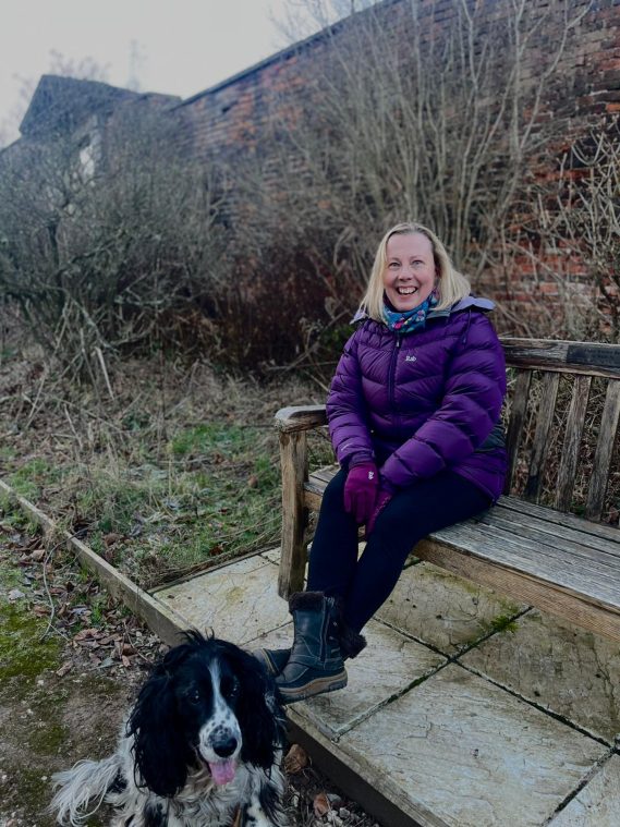 Rebecca sitting on a bench smiling next to her dog.