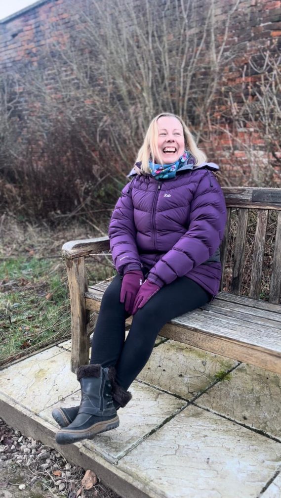 Rebecca from Pilates & Wellness by Rebecca Anne sitting on a bench and laughing.